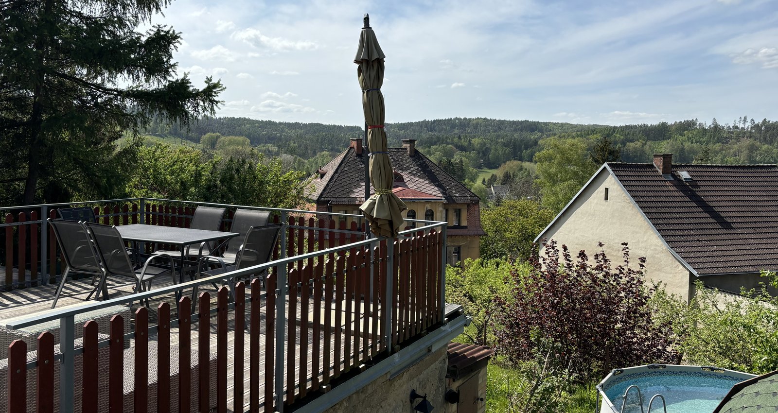 Terrasse mit Blick in die weite Umgebung und Sitzgelegenheiten sowohl unter dem Sonnenschirm als auch auf dem Sofa.